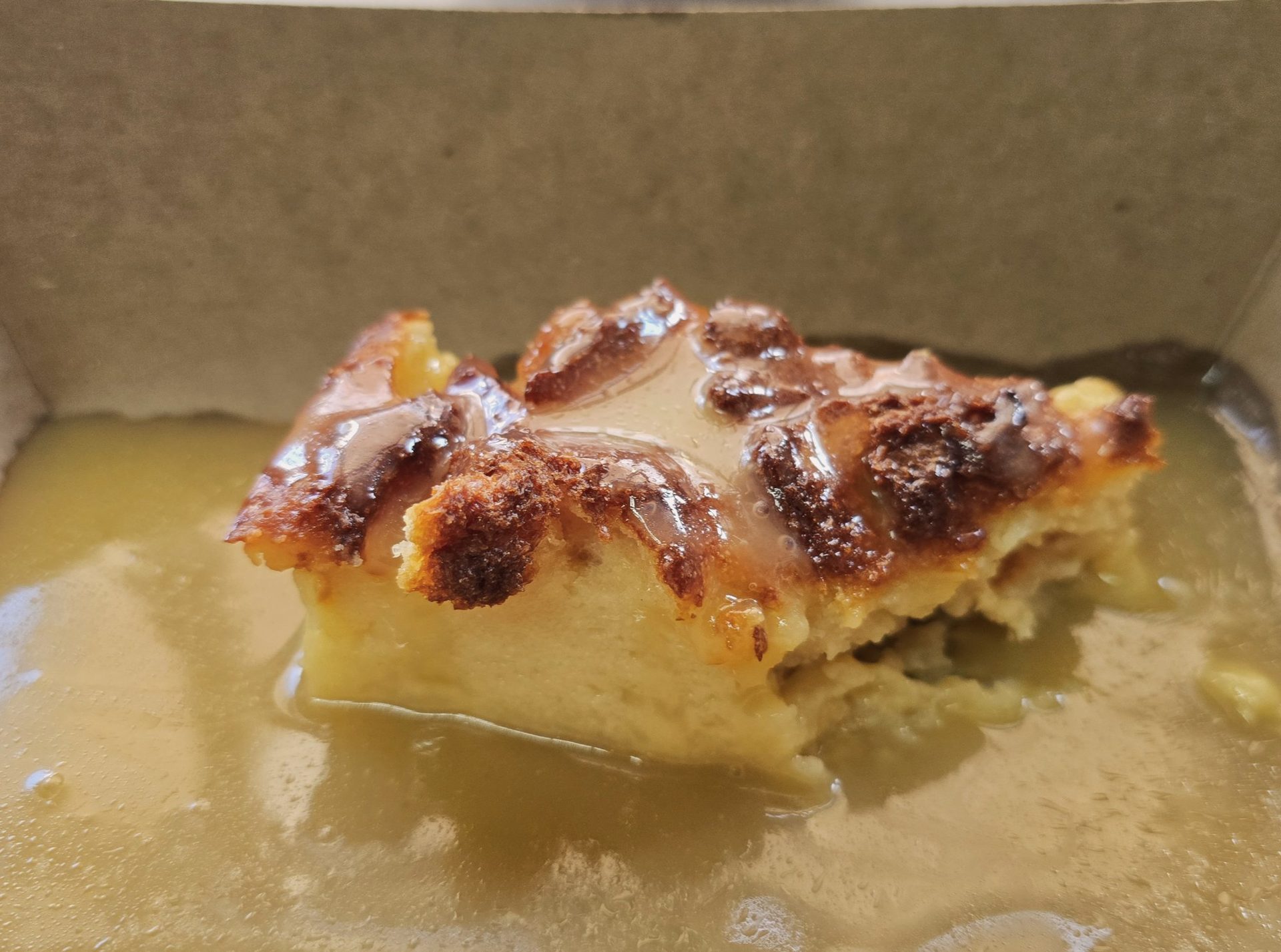 Warm bread pudding served with sauce in a takeout tray